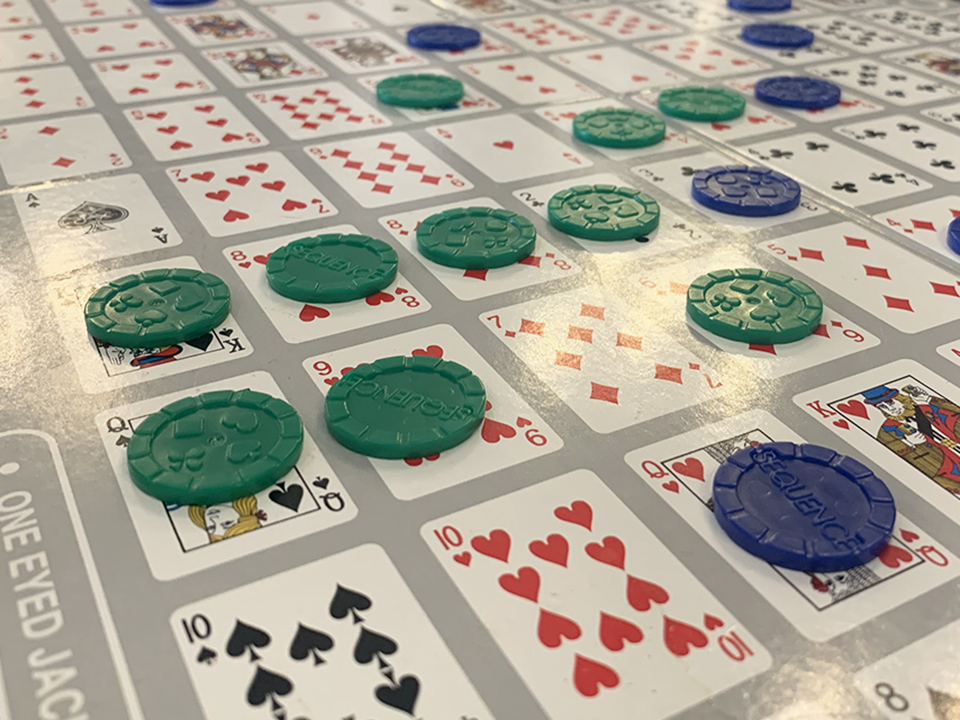 poker chips on sequence game board shows four green chips in a row blocked by a blue chip